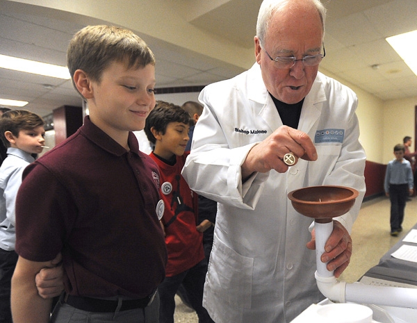 Bishop Richard Malone, wearing a lab coat presented to him by students, tries out the science experiment made by Our Lady of Victory School sixth grader Matthew Viverto during the Diocese of Buffalo 3rd Annual X-Stream Games and Expo. Area Catholic elemen